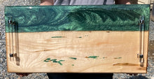 Load image into Gallery viewer, Live Edge Maple, rich warm golds, 100% of wood covered with food safe epoxy, metallic deep green swirls in a horizonal banner pattern with some metallic green highlights below along mid-bottom of board with clear tube handles.

